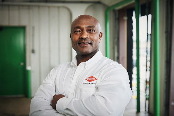 An Orkin Pro standing in a warehouse with his arms crossed over his chest-600x400